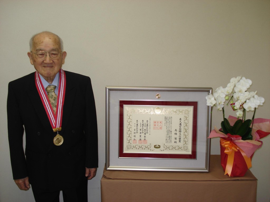 賞状の横に立つ高橋博士の写真